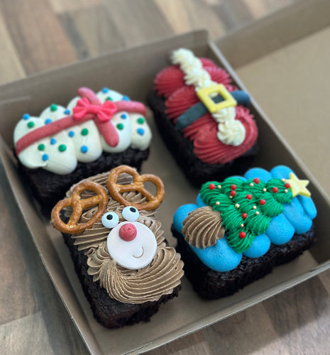 Four festive-themed cupcakes in a box on a wooden surface