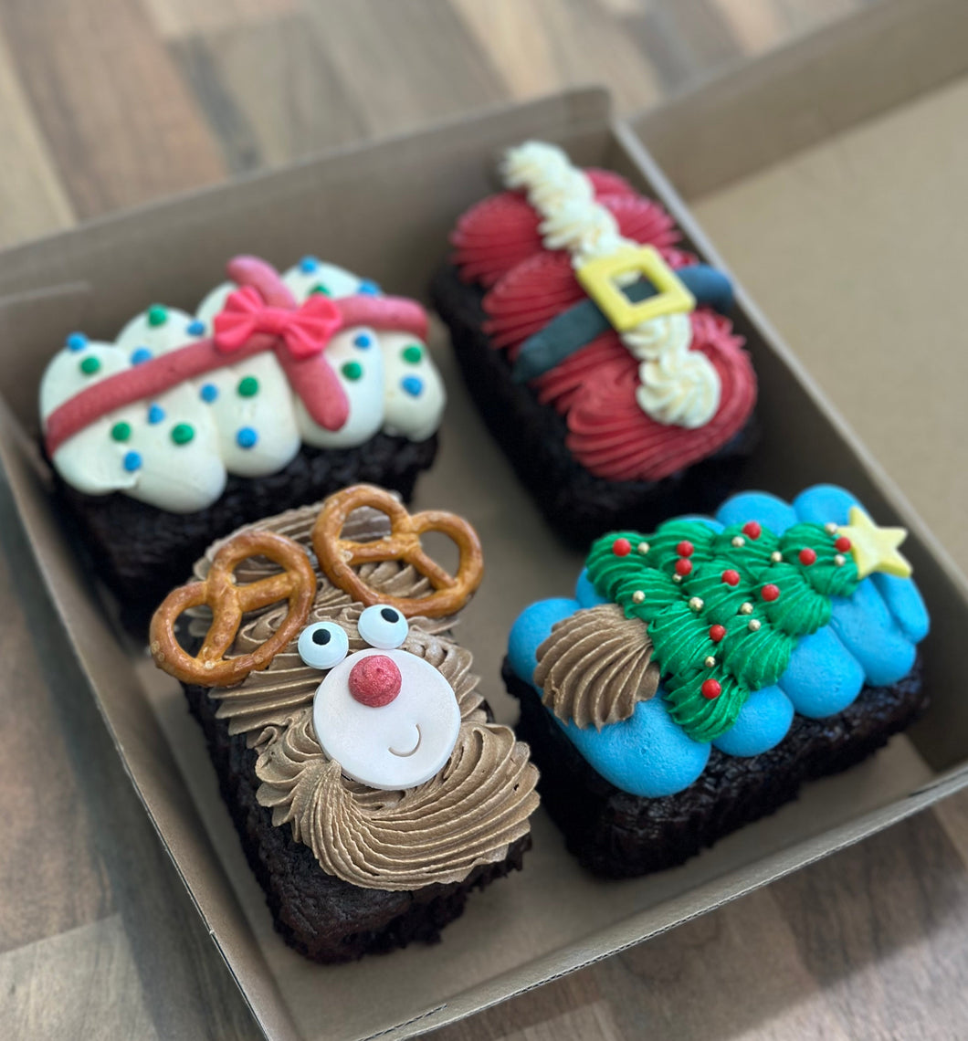Four festive-themed cupcakes in a box on a wooden surface